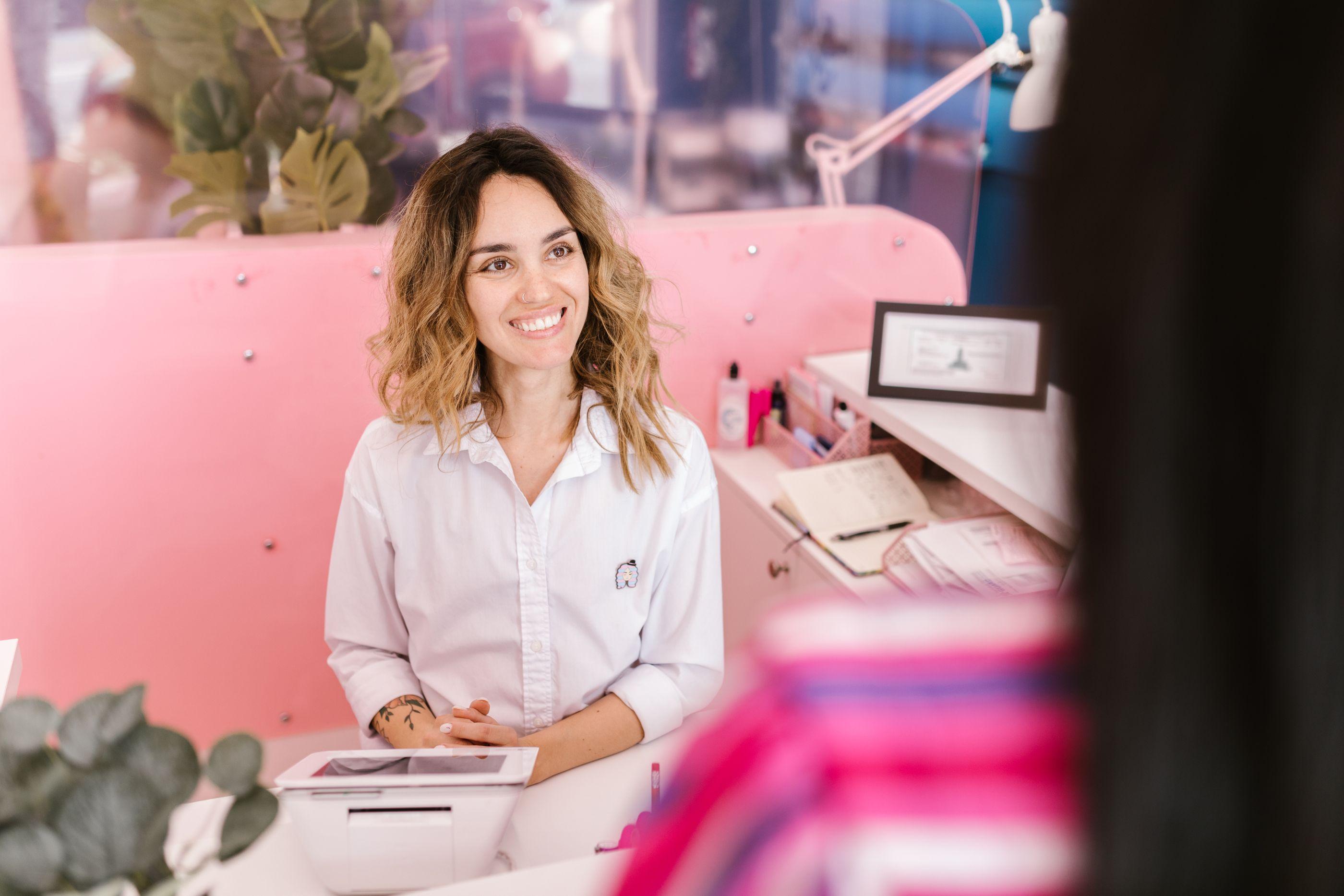 Receptionist at boutique wellness front desk with POS terminal greeting member
